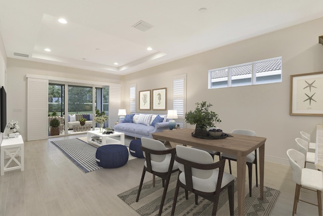 dining area with a raised ceiling and light hardwood / wood-style flooring