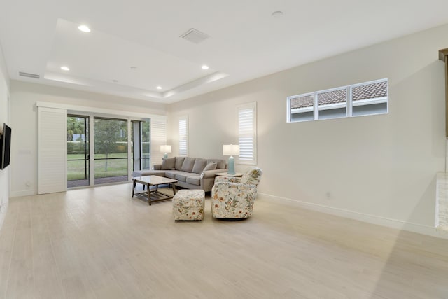 living room featuring a raised ceiling, a wealth of natural light, and light hardwood / wood-style floors