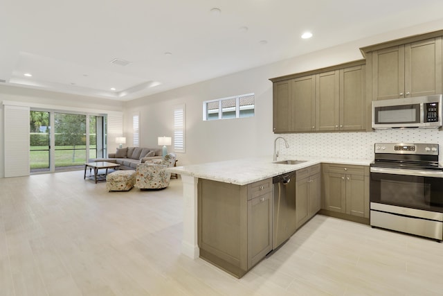 kitchen with sink, kitchen peninsula, a raised ceiling, stainless steel appliances, and light stone countertops