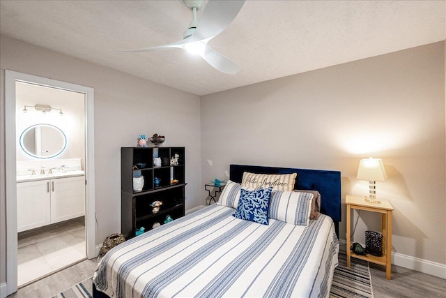 bedroom with light wood finished floors, connected bathroom, a textured ceiling, ceiling fan, and baseboards