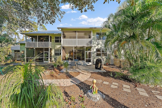 rear view of house featuring a balcony, a sunroom, a patio area, and fence