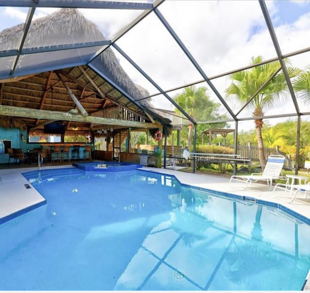 outdoor pool with a patio area, fence, and glass enclosure