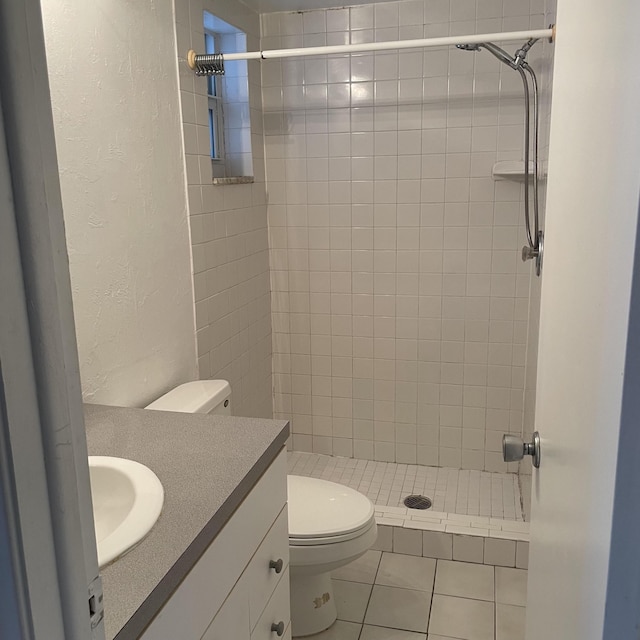 bathroom featuring tile patterned floors, vanity, toilet, and a tile shower