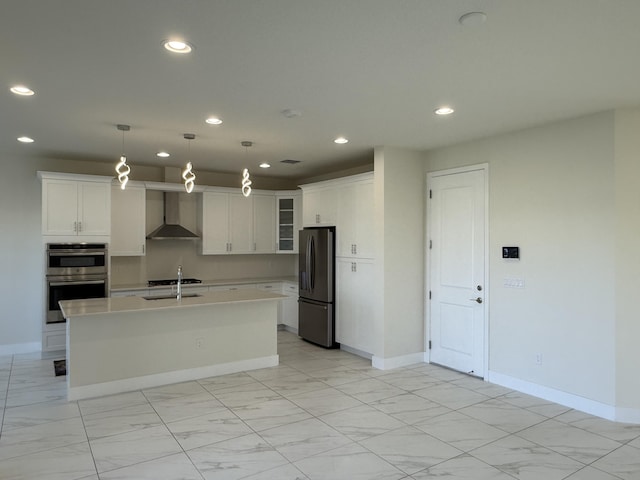 kitchen with a kitchen island with sink, wall chimney range hood, decorative light fixtures, white cabinetry, and stainless steel appliances