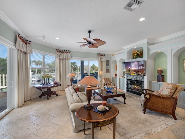 living room with crown molding, a tile fireplace, ceiling fan, and a textured ceiling