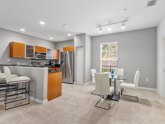 kitchen with light carpet, appliances with stainless steel finishes, kitchen peninsula, track lighting, and a kitchen breakfast bar