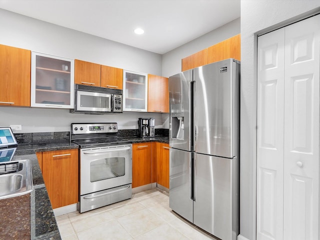 kitchen with appliances with stainless steel finishes, light tile patterned floors, dark stone counters, and sink