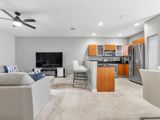 kitchen with ceiling fan, stainless steel appliances, light colored carpet, a breakfast bar area, and a kitchen island