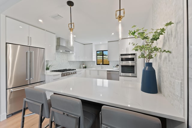 kitchen with white cabinetry, appliances with stainless steel finishes, decorative light fixtures, and wall chimney range hood