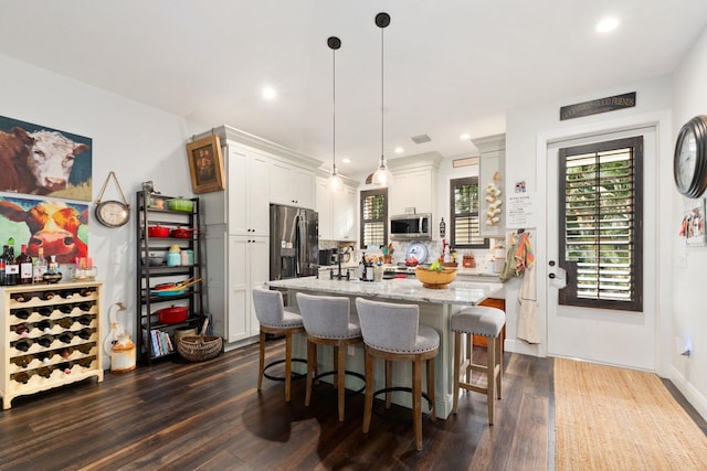 kitchen with white cabinets, light stone counters, appliances with stainless steel finishes, decorative light fixtures, and dark hardwood / wood-style flooring