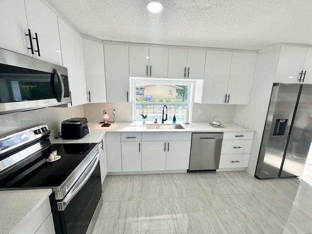 kitchen featuring white cabinets, sink, stainless steel appliances, and a textured ceiling