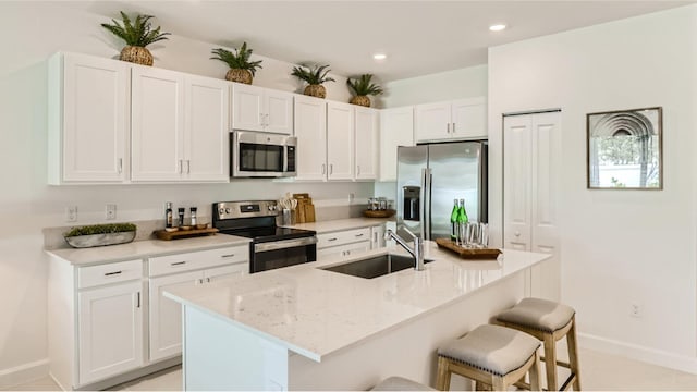 kitchen featuring appliances with stainless steel finishes, a kitchen breakfast bar, sink, white cabinets, and an island with sink