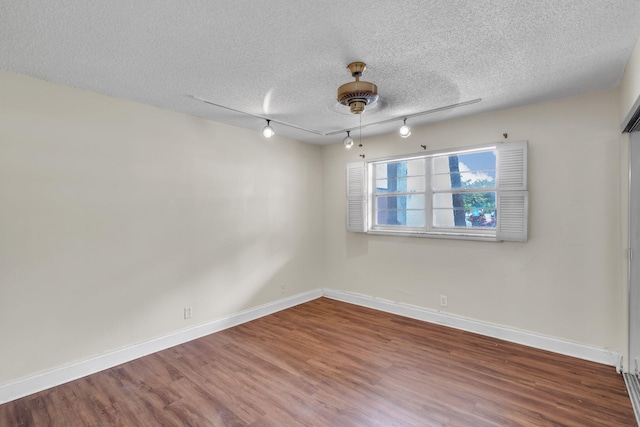 empty room featuring ceiling fan, rail lighting, a textured ceiling, and hardwood / wood-style flooring