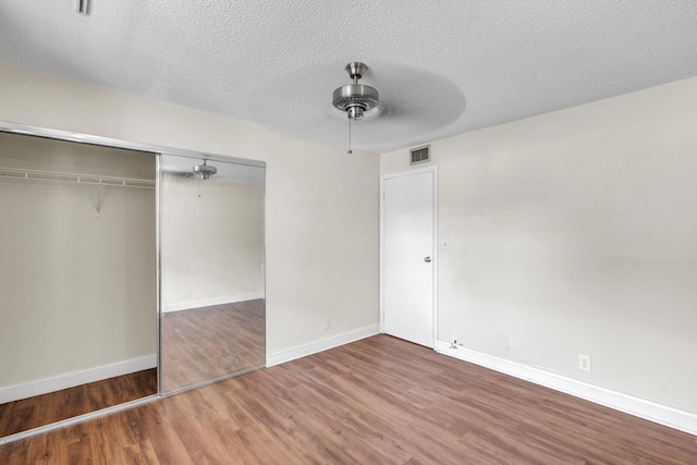 unfurnished bedroom with hardwood / wood-style floors, a textured ceiling, a closet, and ceiling fan