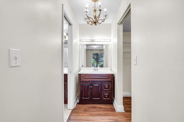 hallway with light hardwood / wood-style floors, sink, a textured ceiling, and an inviting chandelier