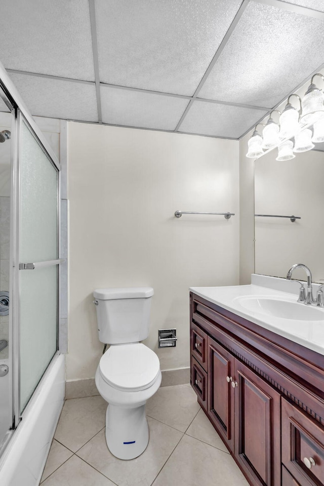 full bathroom featuring tile patterned floors, a drop ceiling, bath / shower combo with glass door, vanity, and toilet