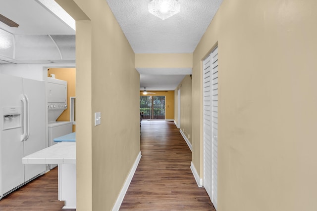 hall featuring a textured ceiling, dark wood-type flooring, and stacked washer and clothes dryer