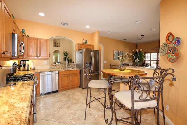 kitchen featuring stainless steel appliances, light tile patterned floors, light stone counters, decorative backsplash, and sink