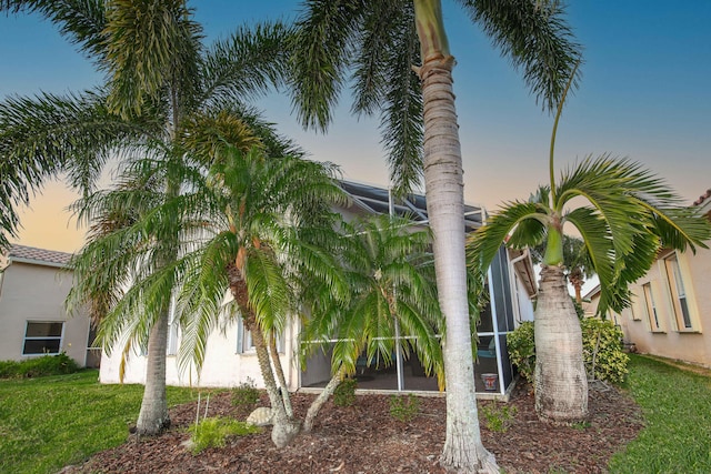 property exterior at dusk with glass enclosure and a yard