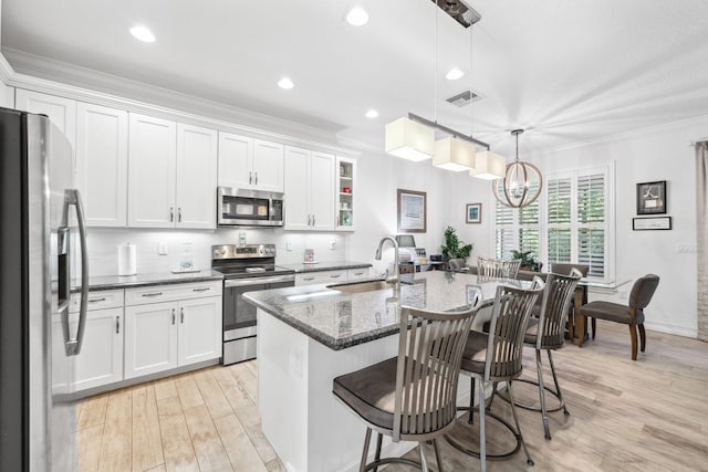 kitchen with a kitchen bar, an island with sink, appliances with stainless steel finishes, hanging light fixtures, and white cabinets