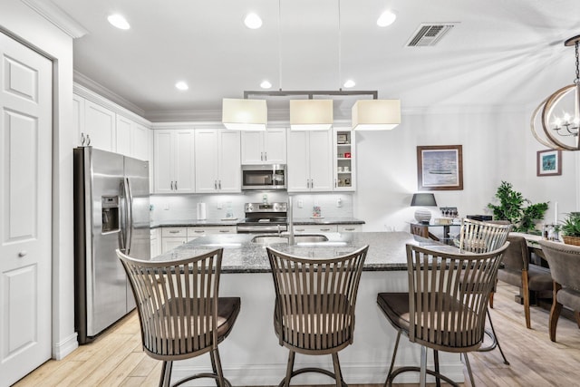 kitchen with decorative light fixtures, appliances with stainless steel finishes, a kitchen breakfast bar, white cabinets, and dark stone counters