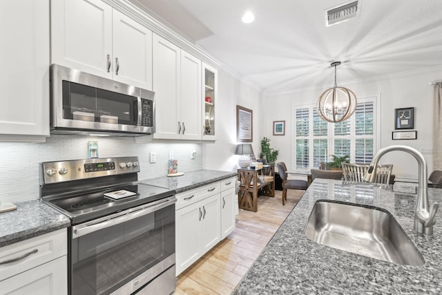 kitchen with appliances with stainless steel finishes, white cabinetry, sink, backsplash, and a chandelier