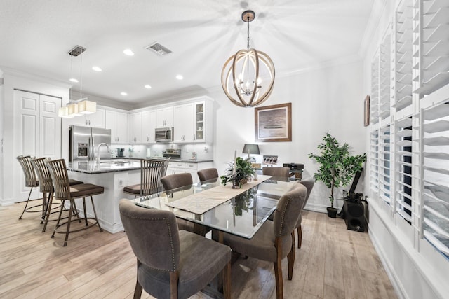 dining space featuring an inviting chandelier, ornamental molding, light hardwood / wood-style flooring, and sink