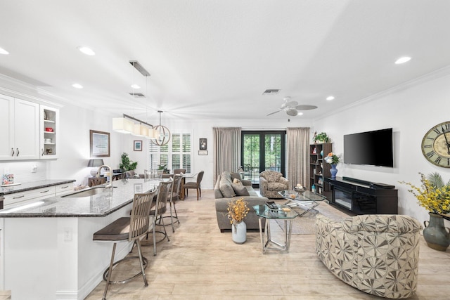 living room with ceiling fan with notable chandelier, sink, ornamental molding, and a fireplace