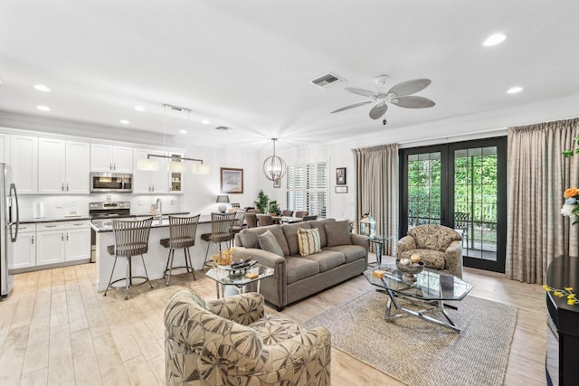 living room featuring ceiling fan with notable chandelier, ornamental molding, and light hardwood / wood-style flooring