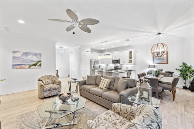 living room featuring light wood-type flooring, crown molding, and ceiling fan with notable chandelier