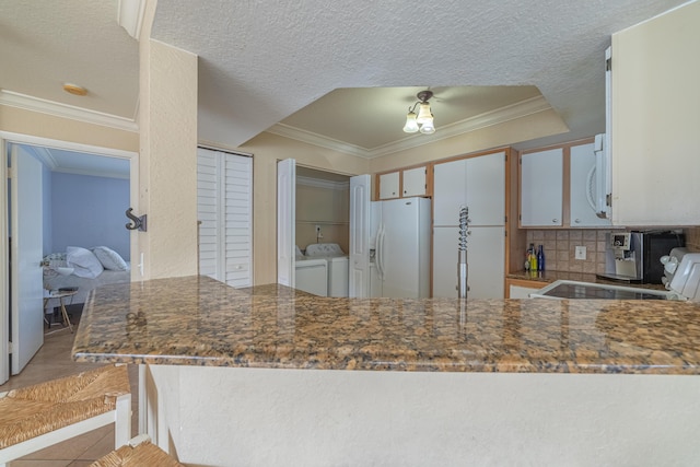 kitchen with light tile patterned floors, white appliances, white cabinetry, washer and dryer, and a textured ceiling