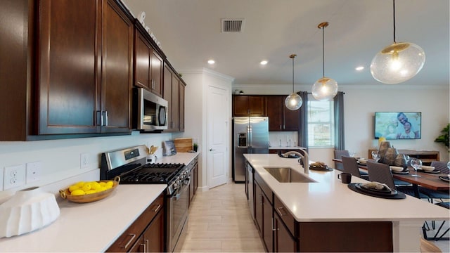 kitchen with a kitchen island with sink, crown molding, sink, hanging light fixtures, and stainless steel appliances