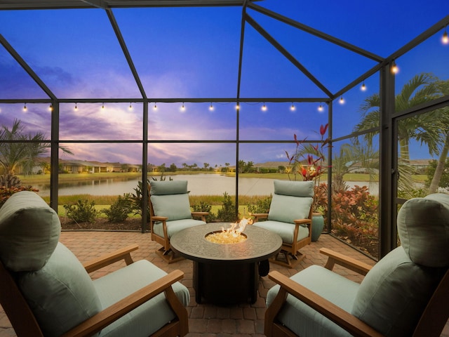 patio terrace at dusk with a water view, a fire pit, and glass enclosure