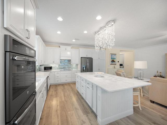 kitchen with light hardwood / wood-style flooring, stainless steel appliances, a center island, tasteful backsplash, and white cabinets