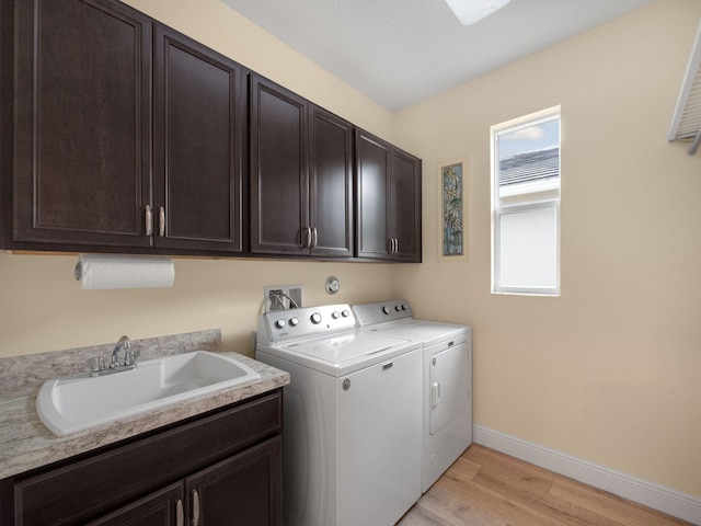 washroom featuring cabinets, sink, washing machine and clothes dryer, and light hardwood / wood-style floors