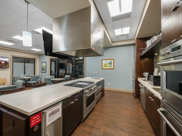 kitchen with appliances with stainless steel finishes, dark hardwood / wood-style flooring, pendant lighting, island exhaust hood, and a drop ceiling