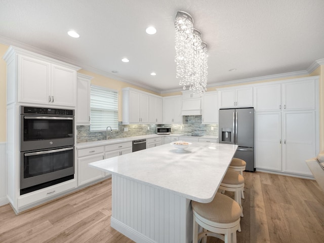 kitchen featuring crown molding, appliances with stainless steel finishes, a kitchen island, and white cabinets