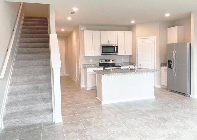 kitchen featuring an island with sink, appliances with stainless steel finishes, light stone countertops, white cabinets, and sink