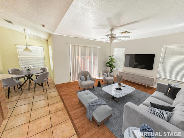 living room featuring a textured ceiling, ceiling fan, tile patterned flooring, and vaulted ceiling