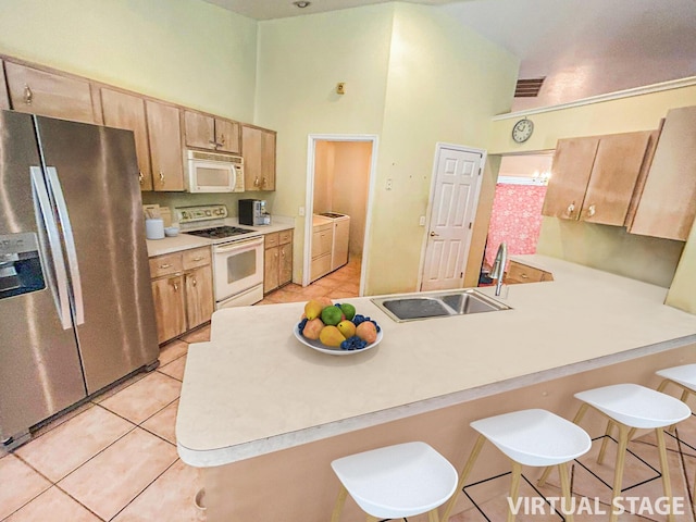 kitchen featuring kitchen peninsula, washer and clothes dryer, a high ceiling, and white appliances