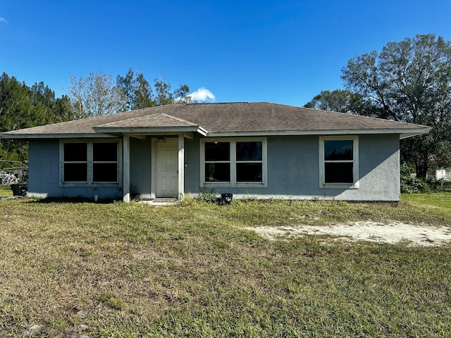 ranch-style home featuring a front lawn, a shingled roof, and stucco siding