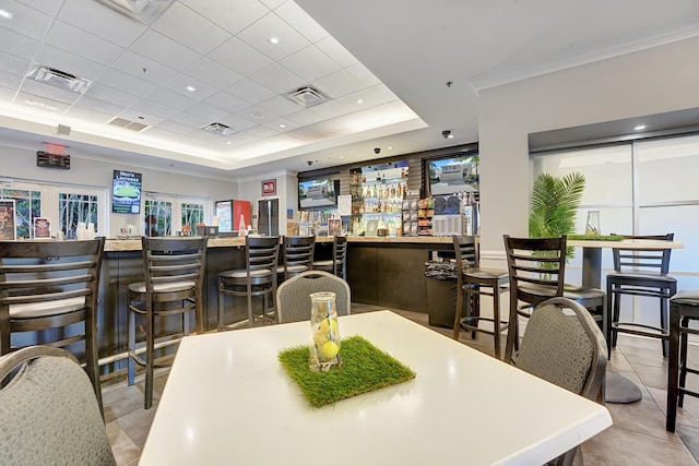 dining area featuring crown molding, a paneled ceiling, bar area, light tile patterned floors, and a raised ceiling