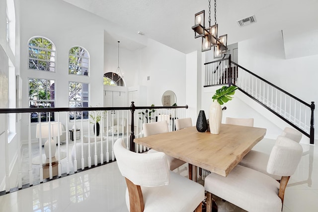 tiled dining area featuring a towering ceiling, a textured ceiling, and an inviting chandelier