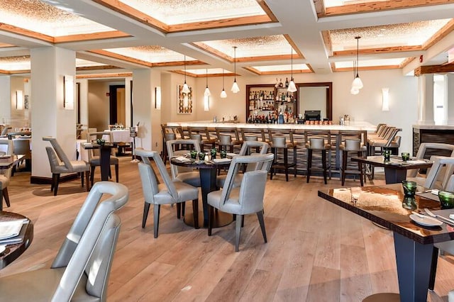 bar with light hardwood / wood-style flooring, beamed ceiling, hanging light fixtures, and coffered ceiling