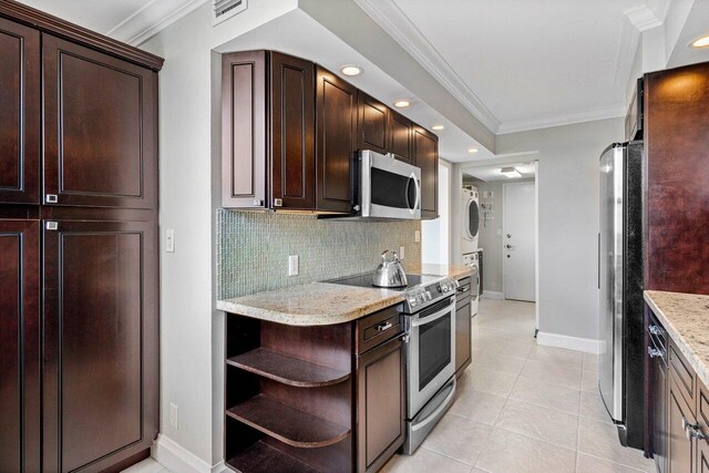 kitchen featuring light stone countertops, appliances with stainless steel finishes, stacked washer and dryer, decorative backsplash, and light tile patterned floors