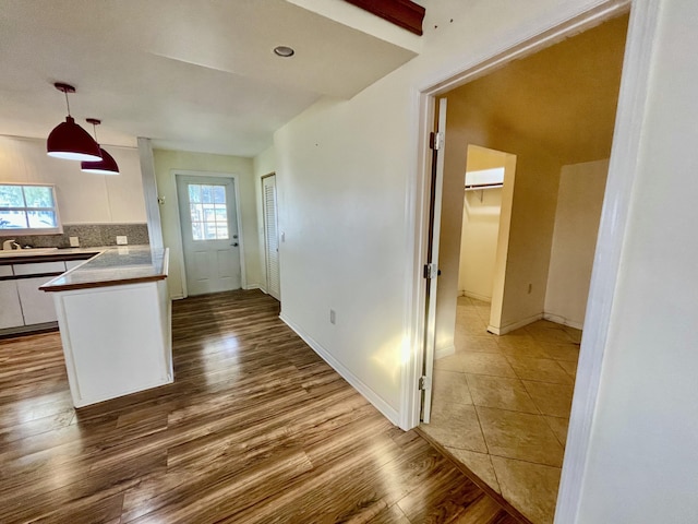 kitchen featuring backsplash, sink, hanging light fixtures, white cabinetry, and wood-type flooring