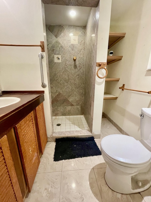 bathroom featuring tile patterned flooring, a tile shower, vanity, and toilet