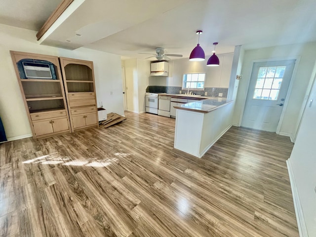 kitchen with backsplash, kitchen peninsula, plenty of natural light, white stove, and light wood-type flooring