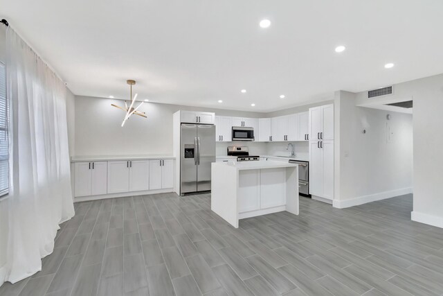 kitchen featuring stainless steel appliances, white cabinetry, plenty of natural light, and a notable chandelier