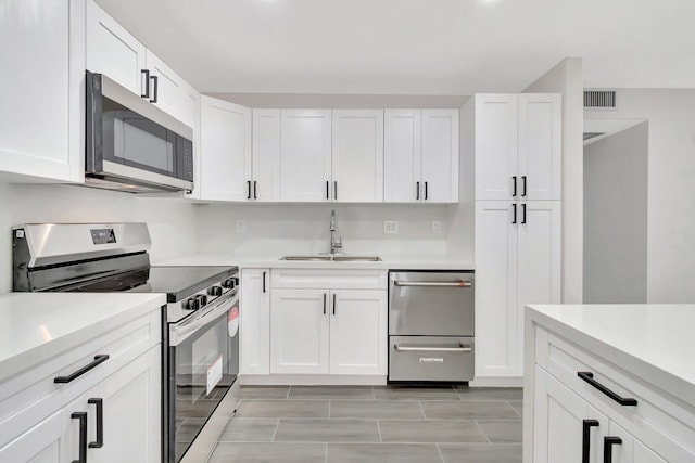 kitchen with light countertops, visible vents, white cabinets, stainless steel appliances, and a sink